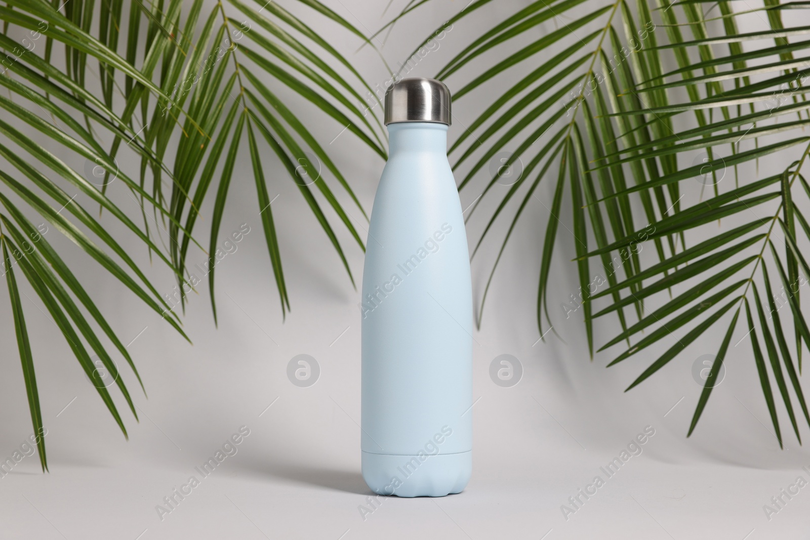 Photo of Stylish thermo bottle near tropical leaves on light grey background