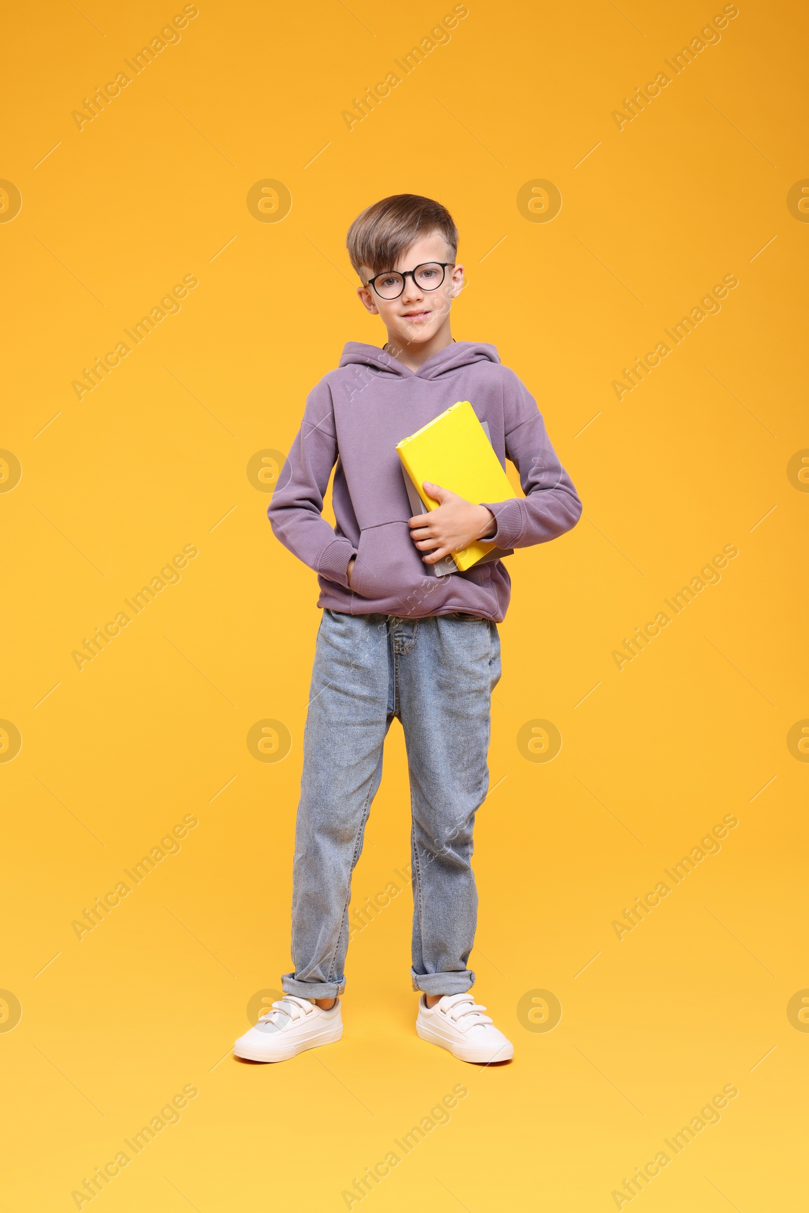 Photo of Cute schoolboy in glasses holding books on orange background