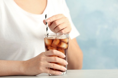 Photo of Woman with glass of tasty refreshing cola at table, closeup view