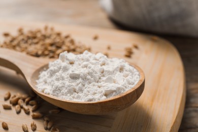 Spoon with wheat flour and grains on wooden board, closeup