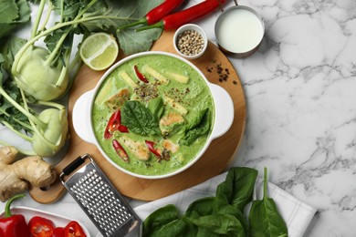 Saucepan with delicious green curry chicken soup and different ingredients on white marble table, flat lay