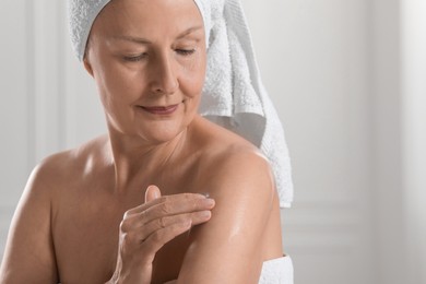 Photo of Happy woman applying body oil onto shoulder indoors. Space for text