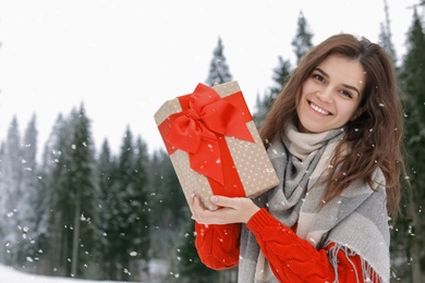 Happy woman with gift box outdoors, space for text. Winter vacation