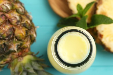 Photo of Tasty pineapple smoothie in bottle, mint and fruit on light blue table, flat lay