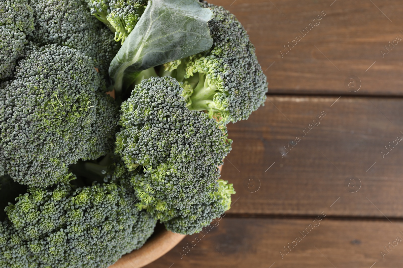 Photo of Bowl with fresh raw broccoli on wooden table, above view and space for text