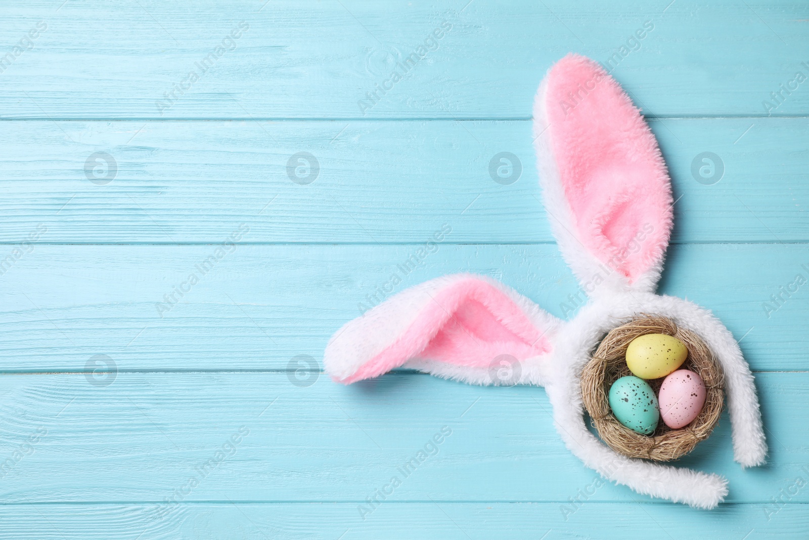 Photo of Headband with bunny ears, painted eggs and space for text on light blue wooden background, flat lay. Easter holiday