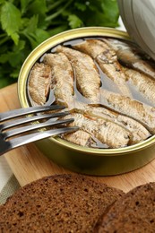 Fork with canned sprats and bread on wooden board, closeup