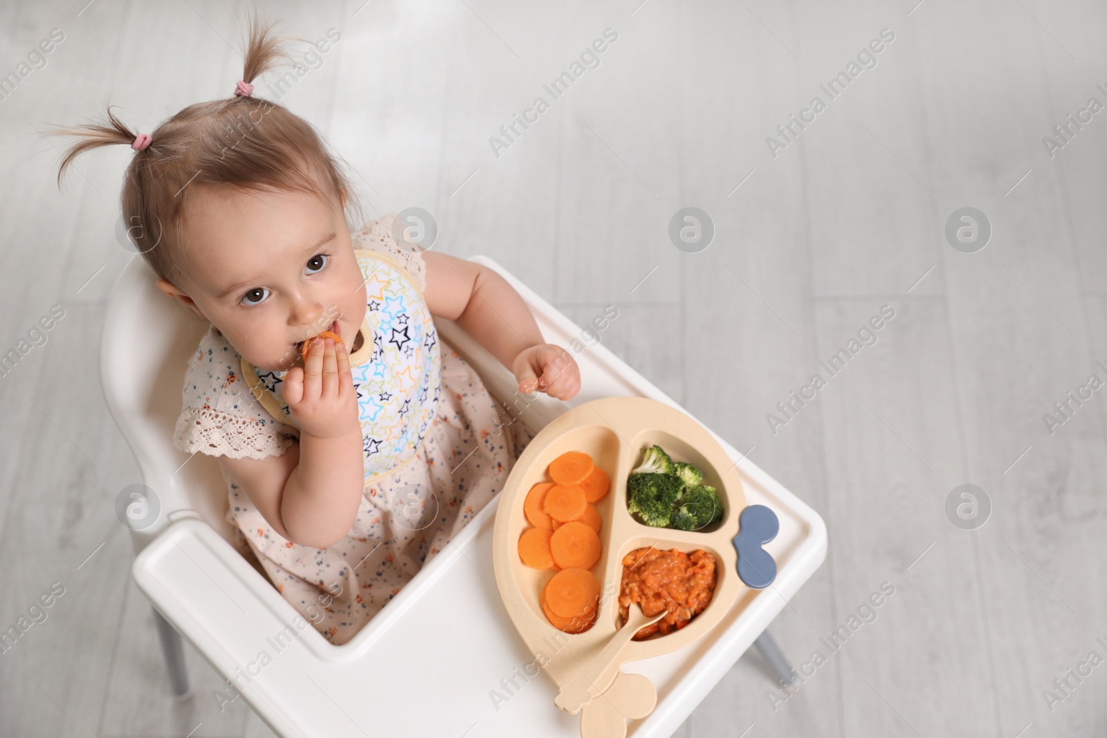 Photo of Cute little baby eating food in high chair indoors, above view. Space for text