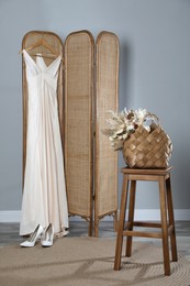 Stylish straw bag with beautiful dried flowers on stool indoors