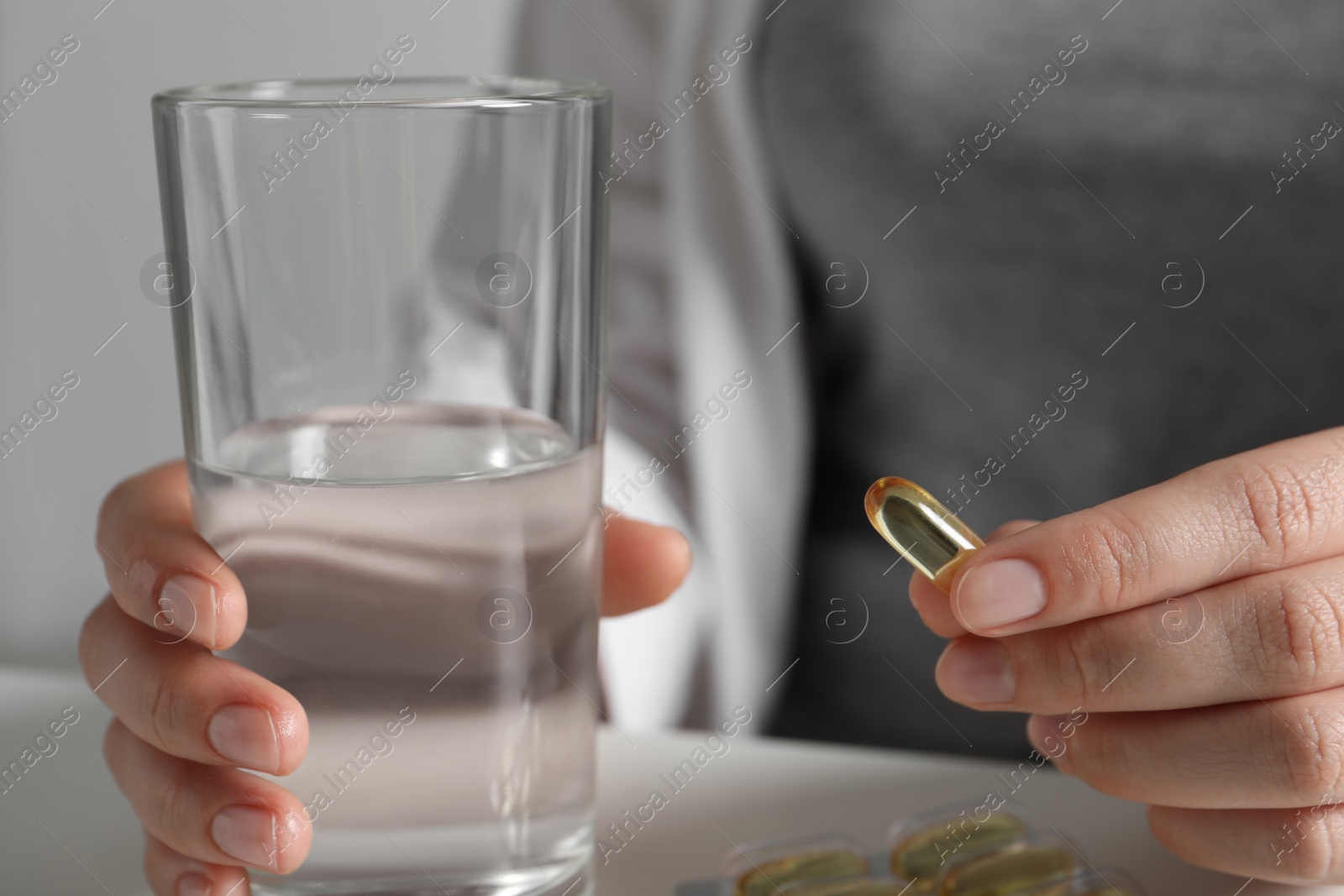 Photo of Woman with glass of water and pill at table, closeup