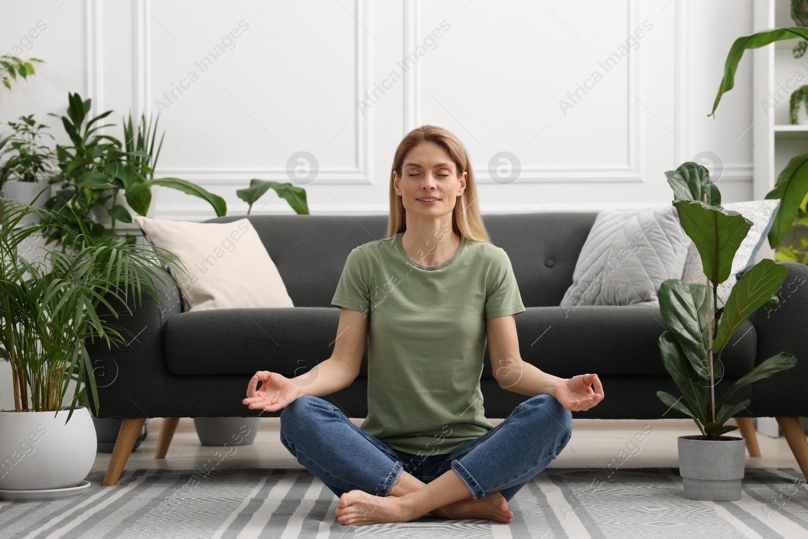 Photo of Woman meditating surrounded by beautiful potted houseplants at home