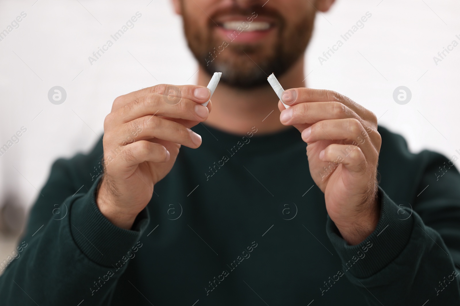Photo of Stop smoking concept. Man holding pieces of broken cigarette on light background, closeup