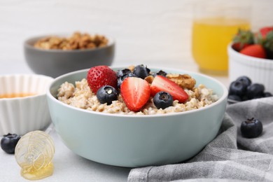 Photo of Tasty oatmeal with strawberries, blueberries and walnuts in bowl on grey table