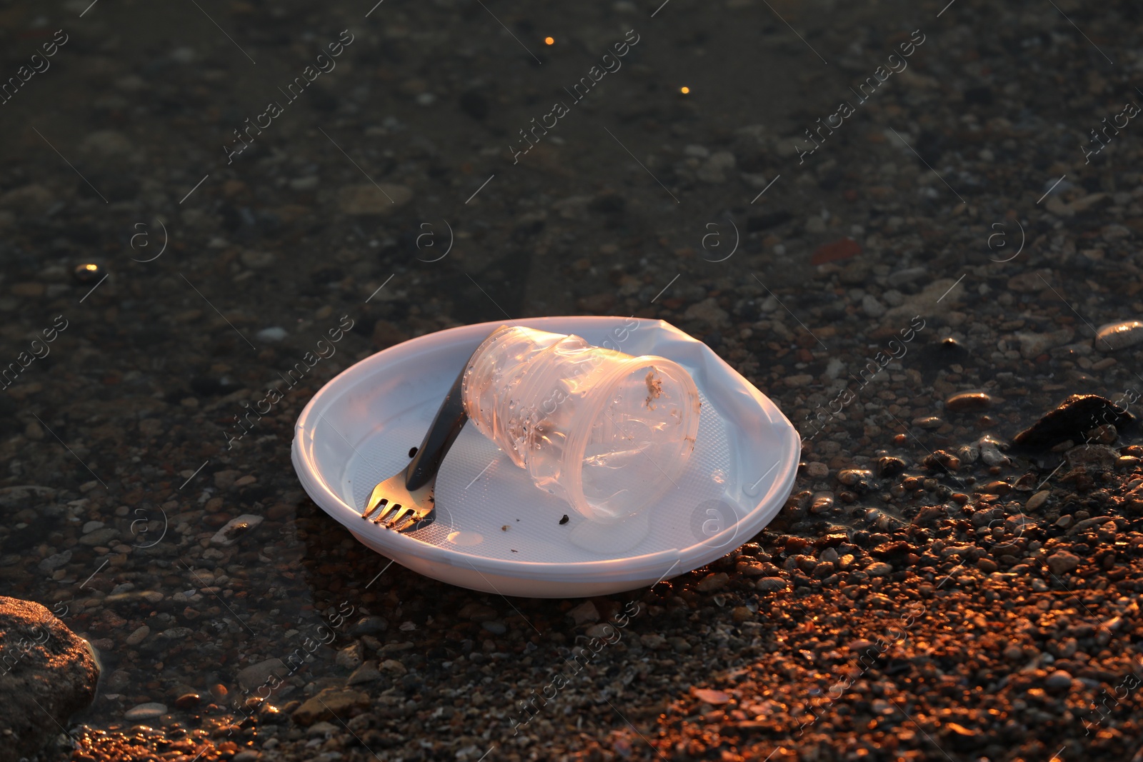 Photo of Used plastic tableware in water outdoors. Environmental pollution concept