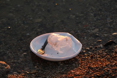 Photo of Used plastic tableware in water outdoors. Environmental pollution concept