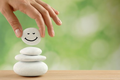 Photo of Woman putting stone with drawn happy face on stack against blurred green background, closeup and space for text. Zen concept