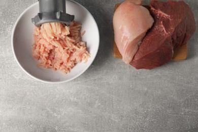 Photo of Metal meat grinder with mince, raw chicken and beef on grey table, flat lay. Space for text