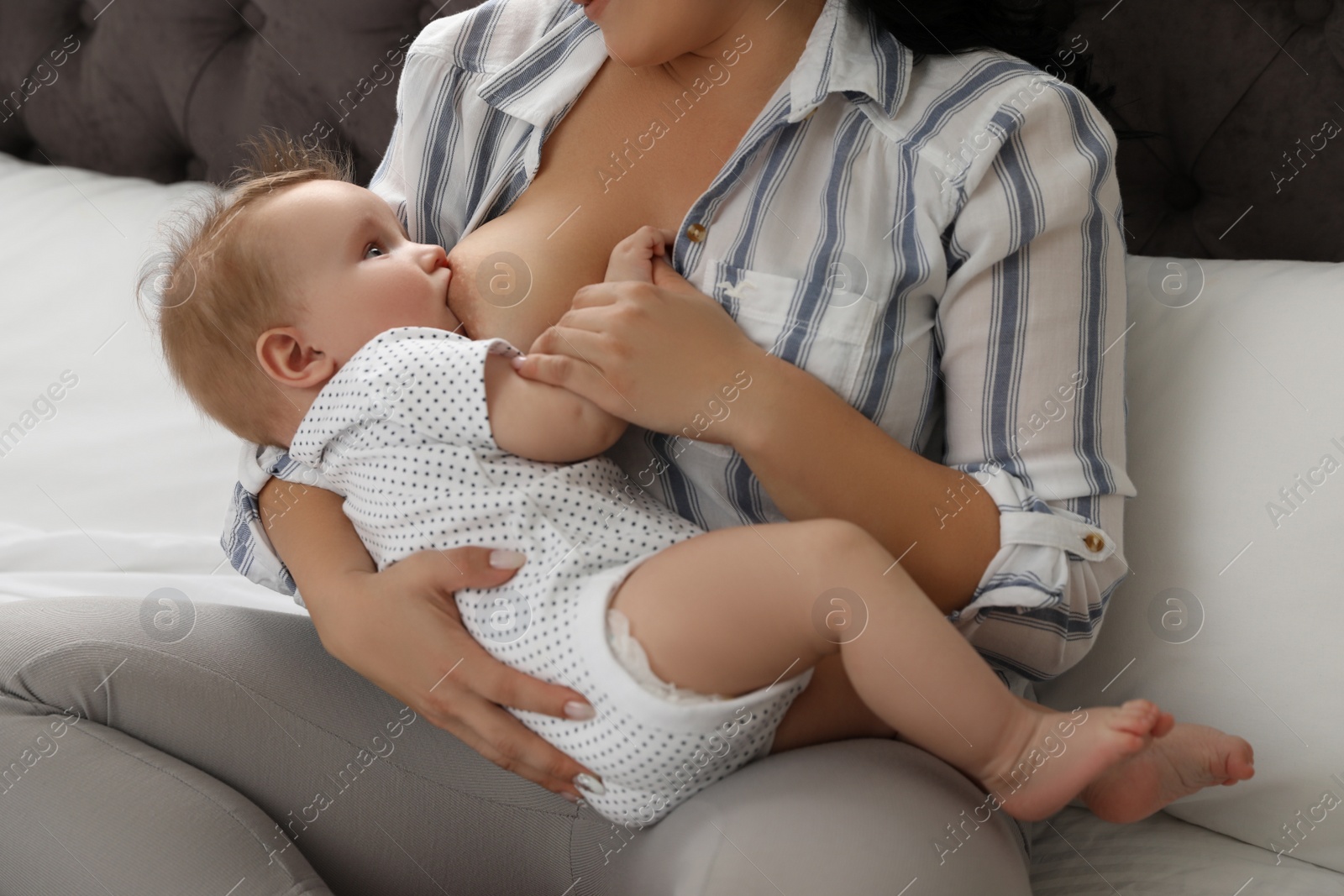 Photo of Woman breastfeeding her little baby on bed indoors