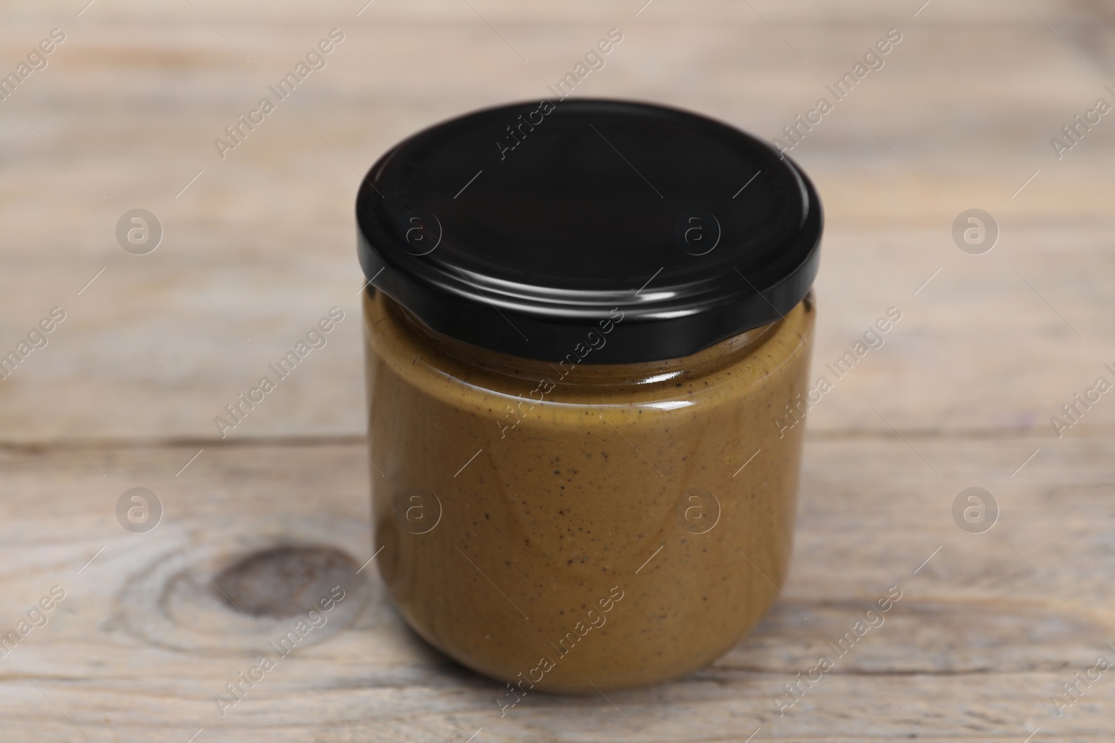 Photo of Tasty nut paste in jar on wooden table, closeup