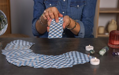 Photo of Fortune teller with deck of tarot cards at grey table indoors, closeup