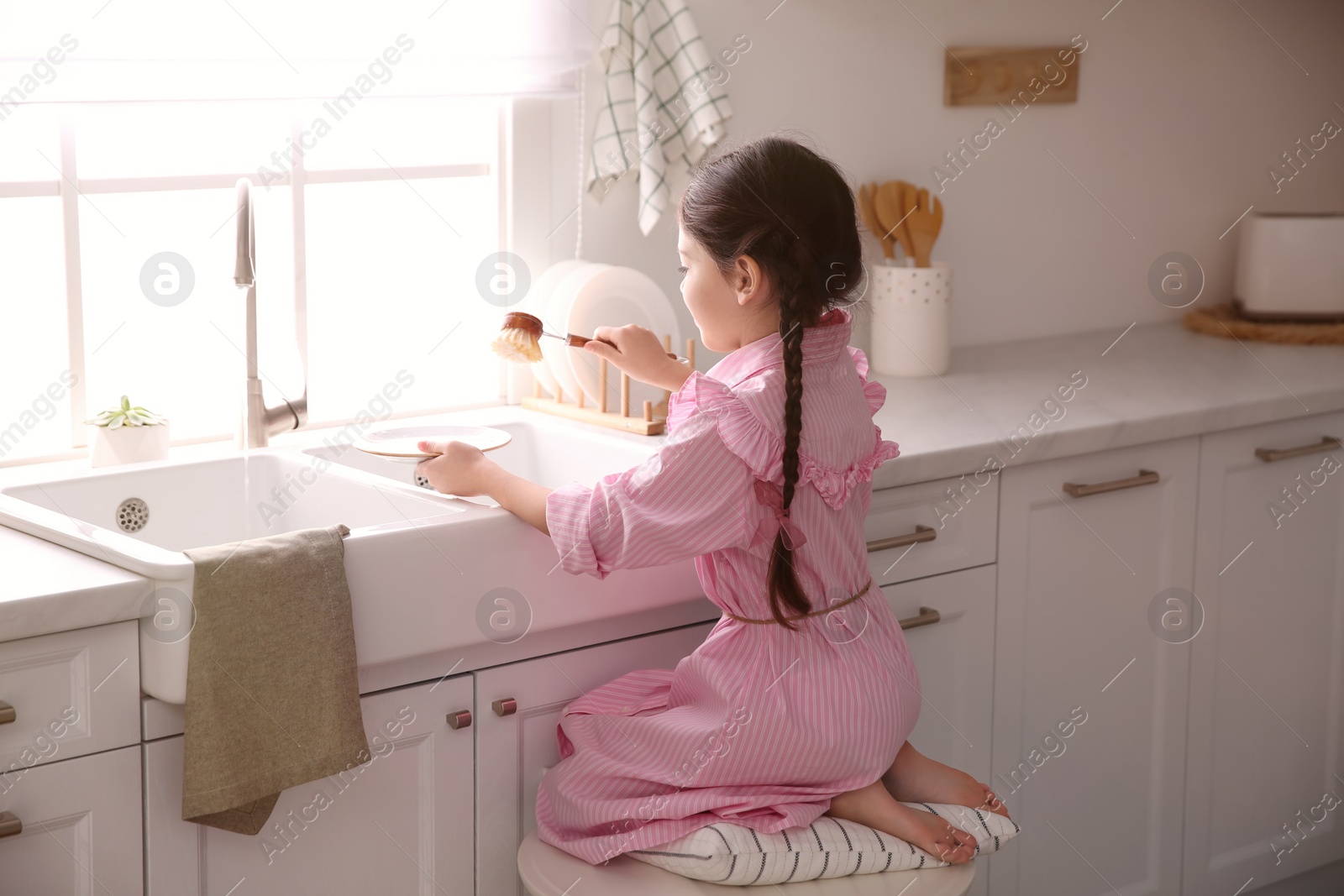 Photo of Little girl washing dishes in kitchen at home