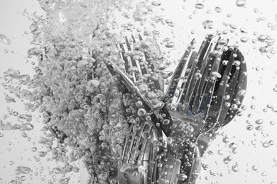 Washing silver cutlery in water on white background, closeup