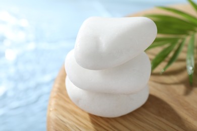 Photo of Spa stones on wooden surface against light blue background, closeup