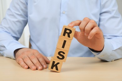 Photo of Businessman destroying tower of cubes with word Risk at table, closeup