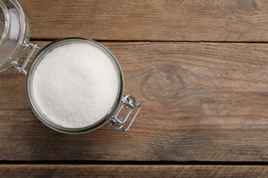 Photo of Granulated sugar in glass jar on wooden table, top view. Space for text