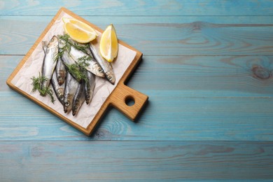 Fresh raw sprats, dill and cut lemon on light blue wooden table, top view. Space for text