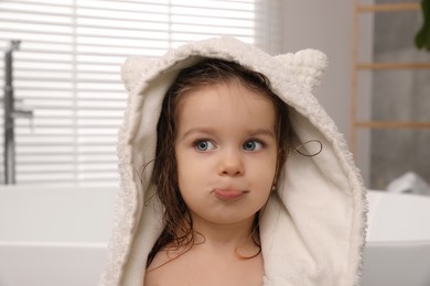 Cute little girl wrapped with hooded towel after washing hair in bathroom