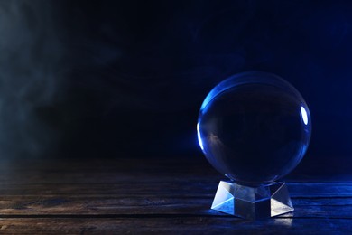 Photo of Magic crystal ball on wooden table against dark background, space for text. Making predictions