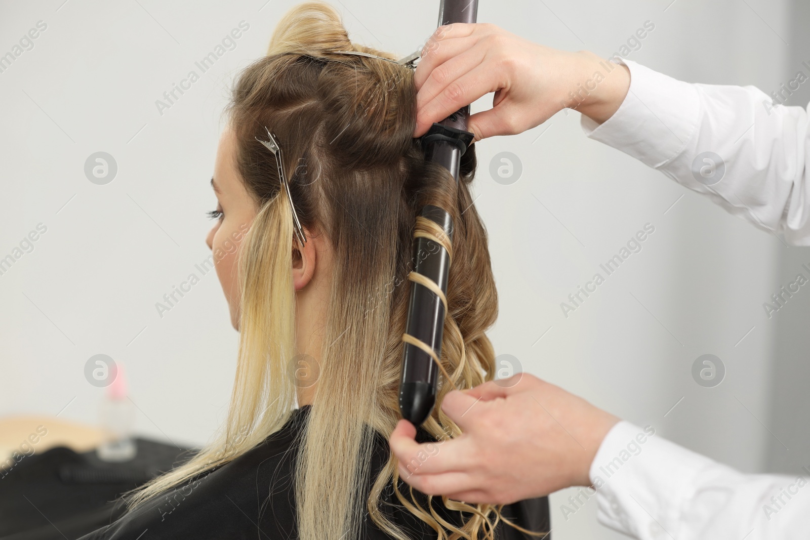 Photo of Hair styling. Hairdresser curling woman's hair in salon, closeup