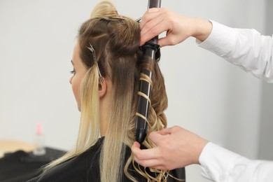 Hair styling. Hairdresser curling woman's hair in salon, closeup