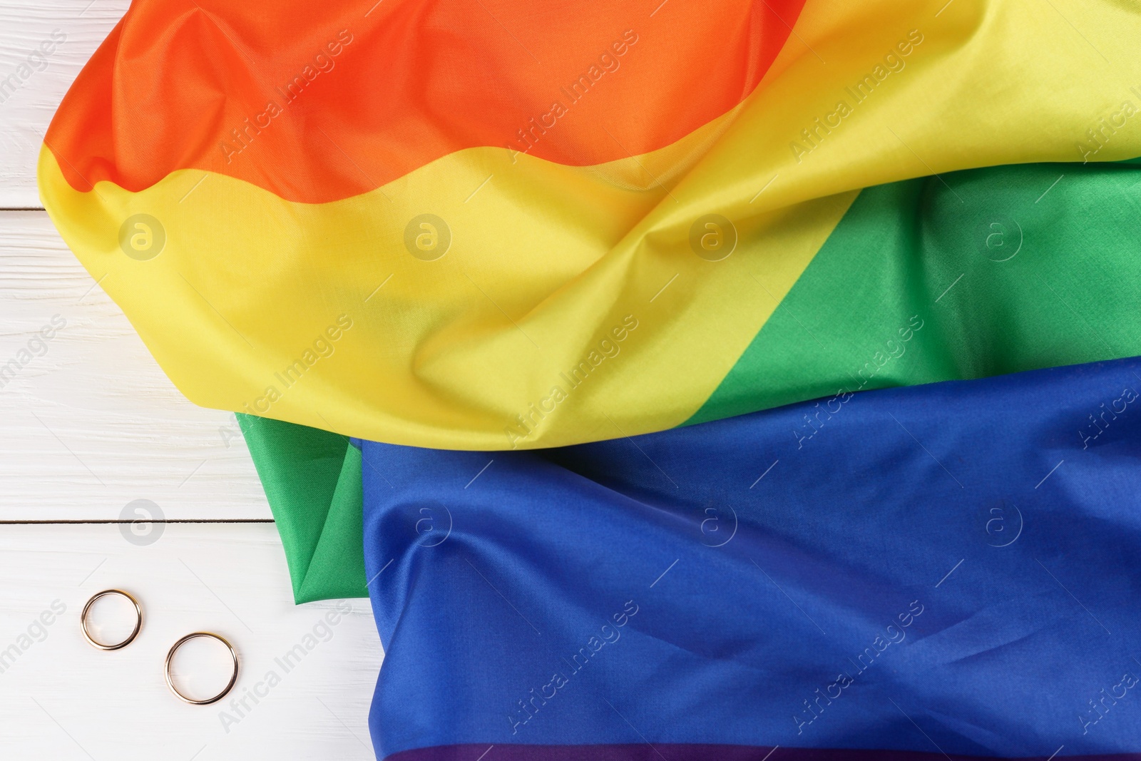 Photo of Rainbow LGBT flag and wedding rings on white wooden table, top view