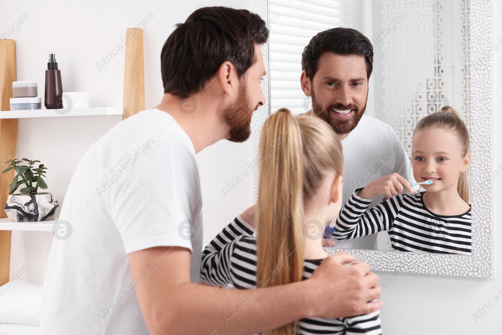 Photo of Father and his daughter brushing teeth together near mirror in bathroom