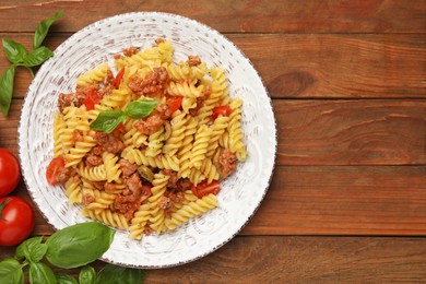 Photo of Plate of delicious pasta with minced meat, tomatoes and basil on wooden table, flat lay. Space for text
