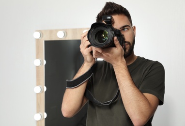 Photo of Young man with professional camera in photo studio. Space for text