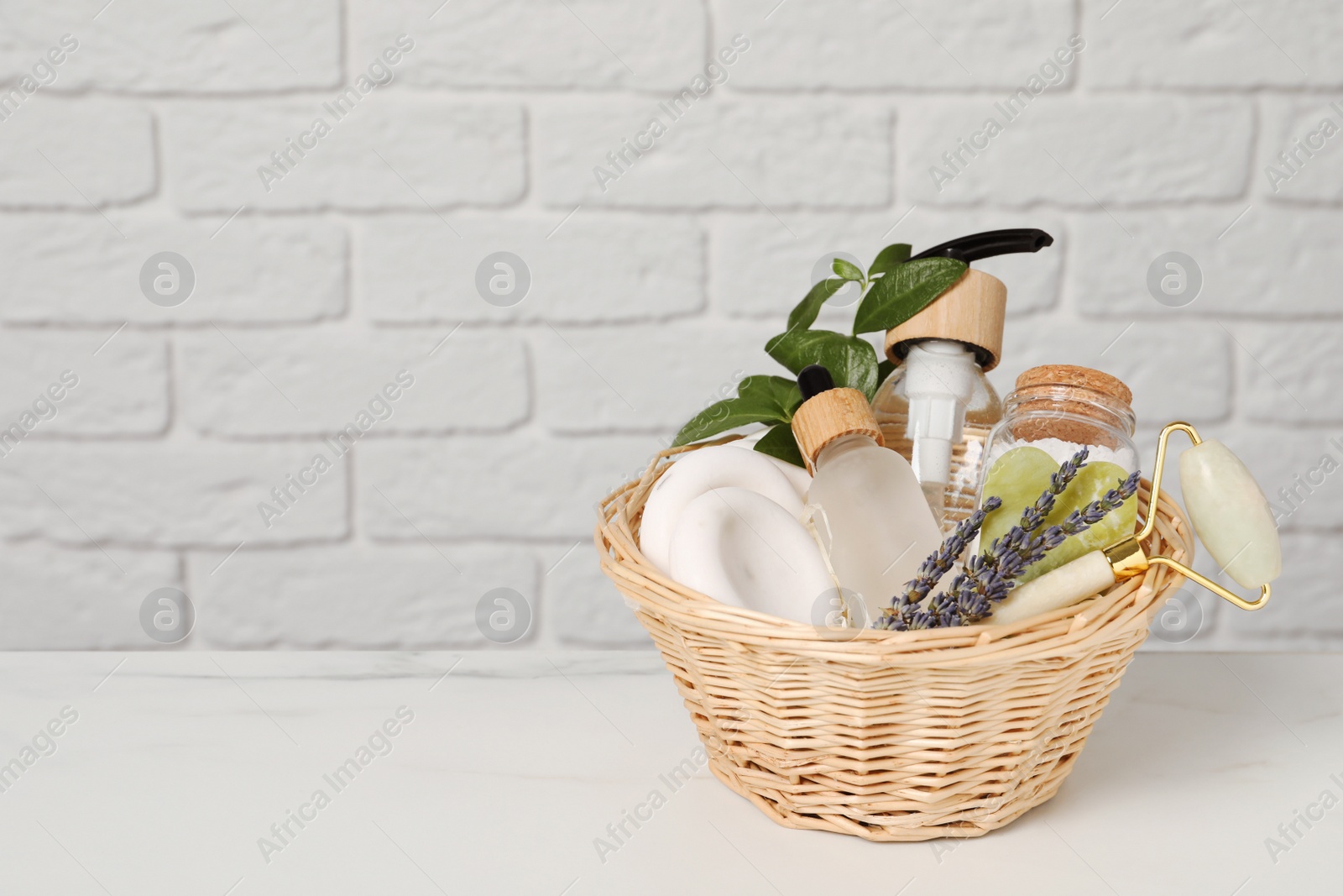 Photo of Spa gift set in wicker basket on white marble table. Space for text