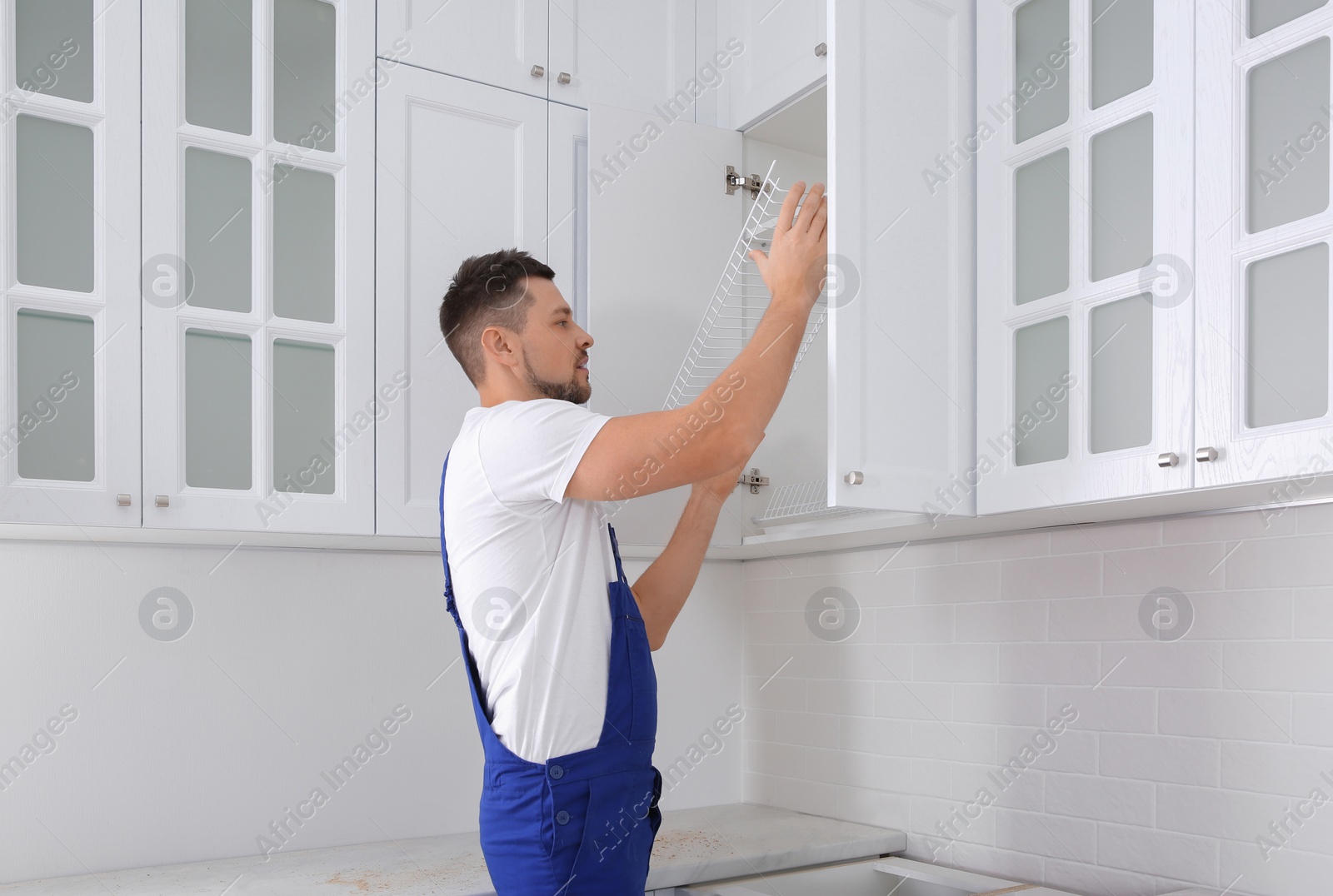 Photo of Worker installing cabinet with shelves in kitchen