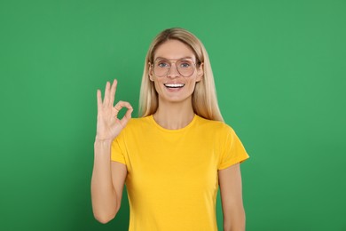 Photo of Happy woman in glasses showing OK gesture on green background