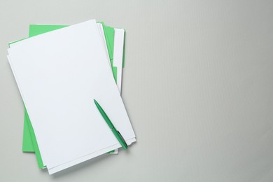 Photo of Green files with blank sheets of paper and pen on light grey background, top view. Space for text