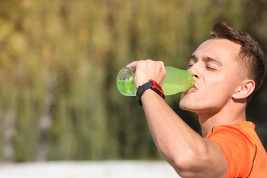 Young sporty man drinking water from bottle outdoors on sunny day. Space for text