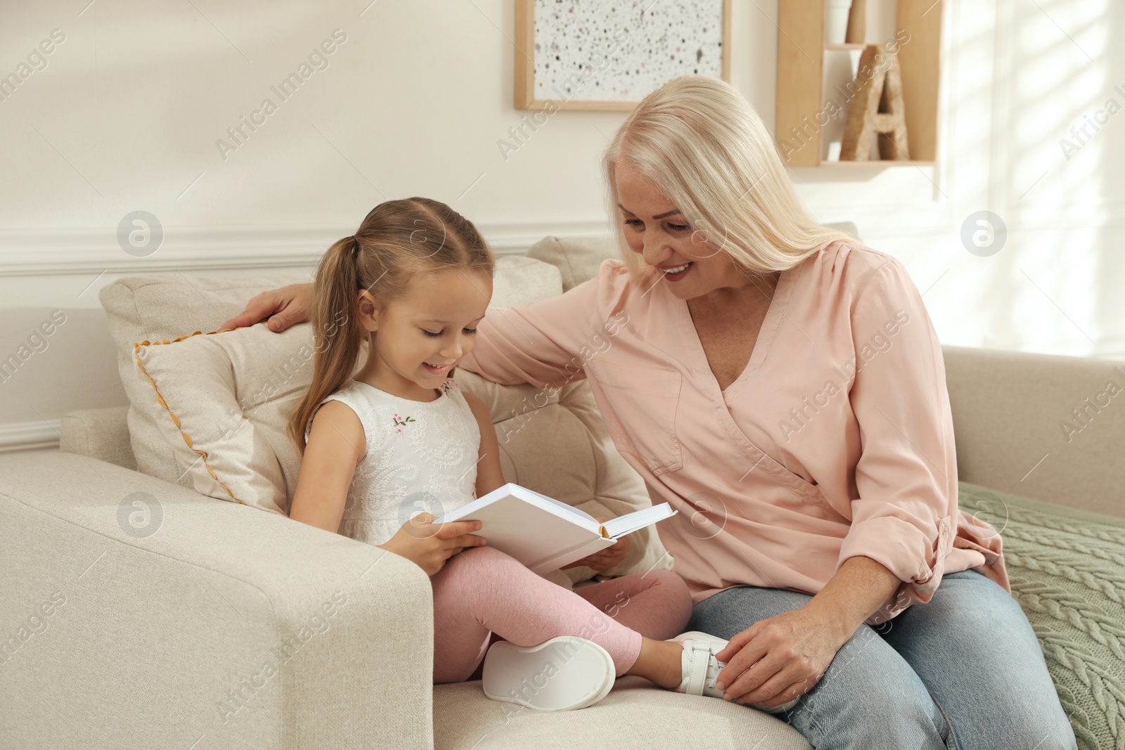 Photo of Happy grandmother with her granddaughter reading book together at home