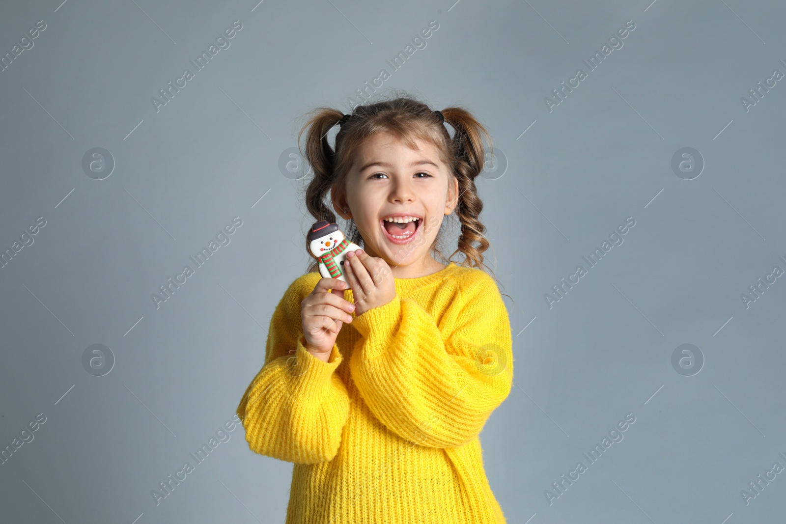 Photo of Cute little girl with Christmas gingerbread cookie on light grey background