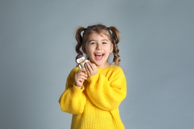 Cute little girl with Christmas gingerbread cookie on light grey background