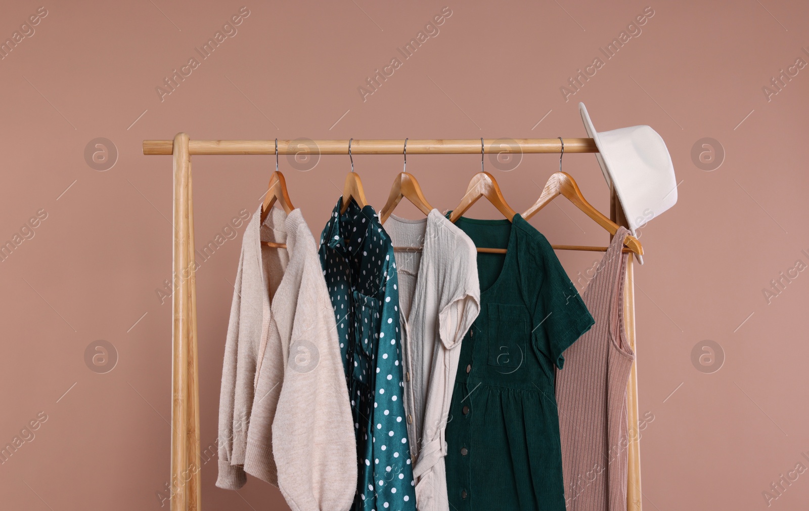 Photo of Rack with hat and stylish women`s clothes on wooden hangers against beige background