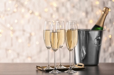 Photo of Glasses with champagne and bottle in bucket on table against blurred lights