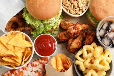 Chips, burgers and other fast food on white wooden table, flat lay