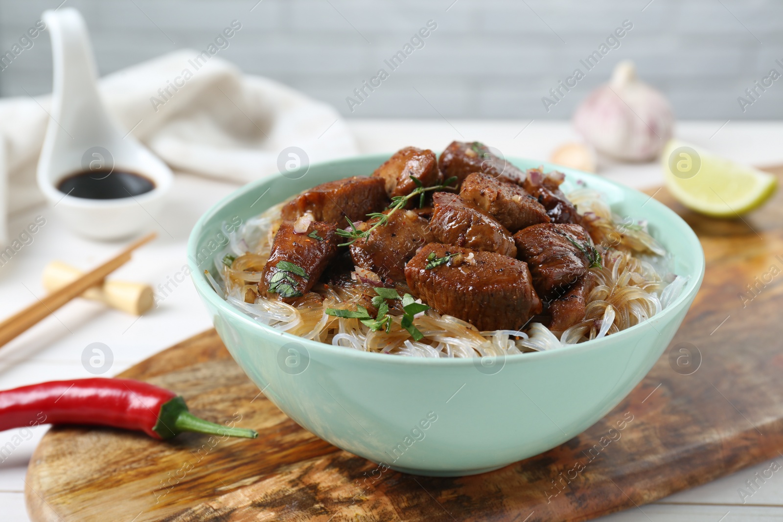 Photo of Bowl with pieces of soy sauce chicken and noodle on white table, closeup